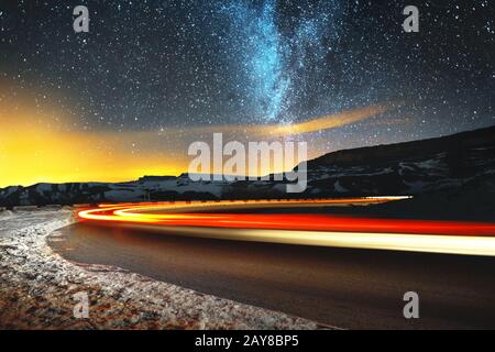 Nachtlandschaft. Nachthimmel mit einer Nordhalbkugel Milchstraße und Sternen. Die vom Auto beleuchtete Nachtstraße schlängelt sich mit einer Serpe Stockfoto