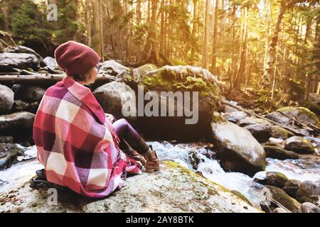 Ein hübsches Mädchen mit einem Pflaster auf den Schultern in einem Hut und einem gelben Pullover und einer Brille mit einem Becher Kaffee in ihr Stockfoto