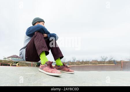 Ein Teenager sitzt auf einem Skateboard im Park. Das Konzept des Zeitvertreibs für Jugendliche in der Stadt Stockfoto