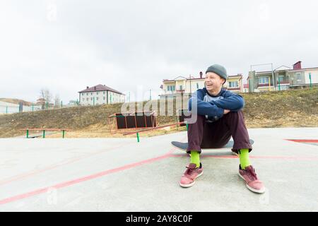 Ein Teenager sitzt auf einem Skateboard im Park und lächelt. Das Konzept des Zeitvertreibs für Jugendliche in der Stadt Stockfoto