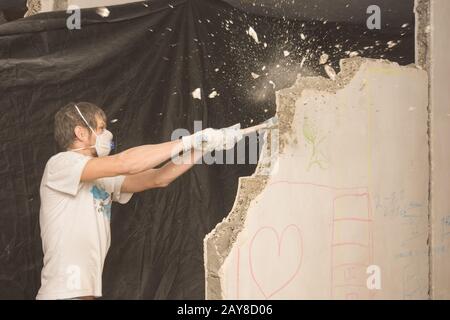 Ein junger Mann bricht eine Partition in der Wohnung mit einem Hammer Stockfoto