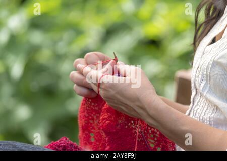 Die Hände einer Frau, die Häkelt mit roter Wolle/strickt Vor unscharfen Hintergrund Stockfoto