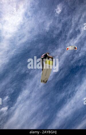 Eine Kiteboarding-Frau springt in die Luft und macht einen Trick zum greifen des Boards, während sie ihren Drachen für eine glatte Landung dreht. Redaktionelle Version. Stockfoto