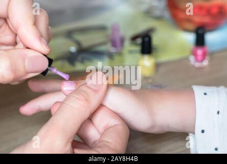 Die Hände einer Frau, die mit einem violetten Nagellack auf die Nägel eines kleinen Mädchens Stockfoto