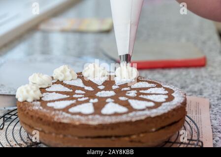 Konditorei schmückt Schokoladenkuchen mit Zuckermuster und Schlagsahne - Nahaufnahme Stockfoto