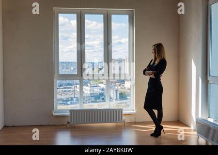 Schlankes Mädchen steht an einem großen Glasfenster in einem leeren Raum Stockfoto