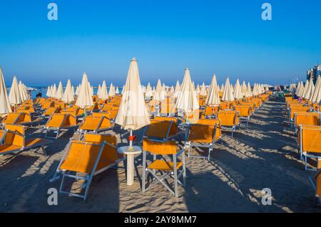 Reihen von orangefarbenen Sonnenschirmen und Liegestuhlen am Strand Stockfoto