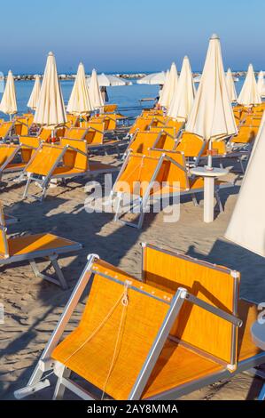 Reihen von orangefarbenen Sonnenschirmen und Liegestuhlen am Strand Stockfoto