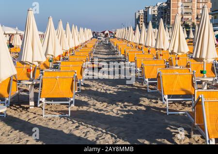 Reihen von orangefarbenen Sonnenschirmen und Liegestuhlen am Strand Stockfoto