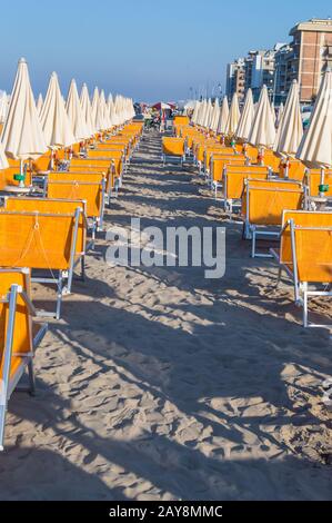 Reihen von orangefarbenen Sonnenschirmen und Liegestuhlen am Strand Stockfoto