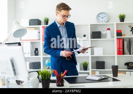 Ein junger Mann steht in der Nähe eine Tabelle im Büro und hält einen Stift und Dokumente. Stockfoto