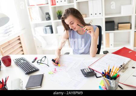 Schöne junge Mädchen im Büro sitzt an einem Tisch, hält in der Hand eine gelbe Markierung und einem Bleistift. Stockfoto