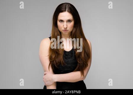 Attraktive Junge ernsthaft wütend brunette kaukasischen Business Woman in Black Dress isoliert auf Grau Stockfoto