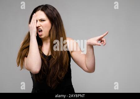 Emotionale ziemlich zuversichtlich wütend Plus size Model im Studio mit Ekel Zeichen auf grauem Hintergrund Stockfoto