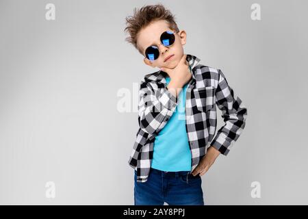 Ein gutaussehender Junge in einem Kraghemd, blauem Hemd und Jeans steht auf grauem Hintergrund. Der Junge trägt eine runde Brille. Rothaarig Stockfoto