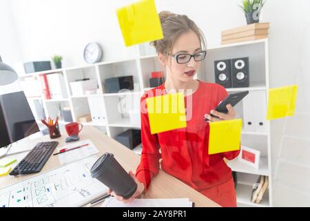 Ein junges Mädchen steht in der Nähe eine transparente Board mit Aufklebern und hält ein Glas mit Kaffee und Telefon. Stockfoto