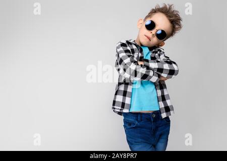 Ein gutaussehender Junge in einem Kraghemd, blauem Hemd und Jeans steht auf grauem Hintergrund. Der Junge trägt eine runde Brille. Rothaarig Stockfoto