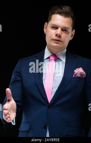 Portrait von zuversichtlich gut aussehender Geschäftsmann mit seiner Hand für Handshake auf schwarzem Hintergrund Stockfoto