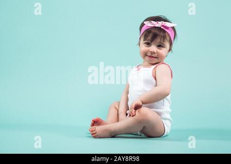 Süße kleine lächelnde Mädchen mit rosa Schleife im Haar sitzen im Studio posiert auf blauem Hintergrund Stockfoto