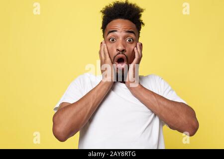 Emotionales und Menschliches Konzept - Porträt eines aufgeregten jungen afroamerikanischen Mannes, der in Erschütterungen und Verwunderung schreit und die Hände an sich hält Stockfoto