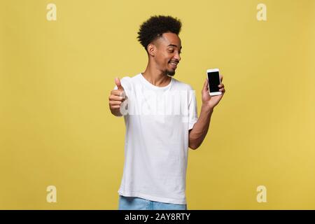 Portrait von fröhlichen afrikanische amerikanische Mann auf Handys mit Daumen nach oben hand Zeichen Stockfoto