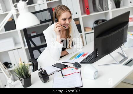 Ein junges Mädchen in Kopfhörer mit Mikrofon sitzt an einem Tisch im Büro und sieht auf dem Monitor. Stockfoto