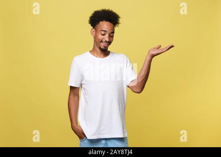 Charmant hübscher junger schwarzer Mann seine Hand bis Betrieb vorhanden Produkt verkaufen zu zeigen. Auf gelben Hintergrund. Stockfoto