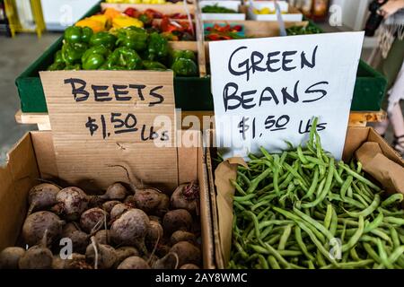 Nahaufnahme von zwei Kartonbehältern mit Gemüse auf dem Lebensmittelmarkt. Schriftliche Preisschilder auf Kartonplatten anhängen. Rüben und grüne Bohnen im Angebot. Stockfoto