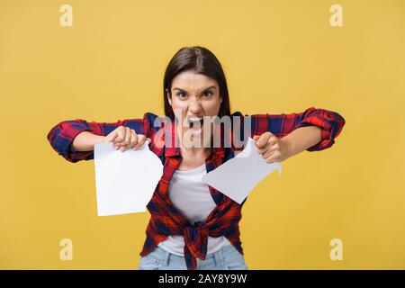 Aggressive jungen kaukasischen Frau tränen Vertrag oder weißes Blatt Papier. Auf gelben Hintergrund. Stockfoto