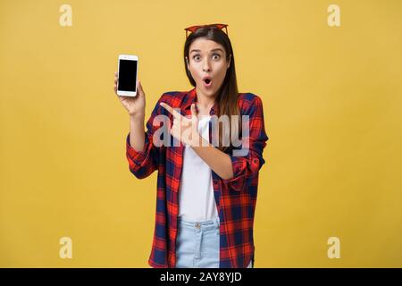 Porträt einer überrascht Frau in casual Tuch mit leerer Bildschirm Mobiltelefon über gelben Hintergrund isoliert Stockfoto