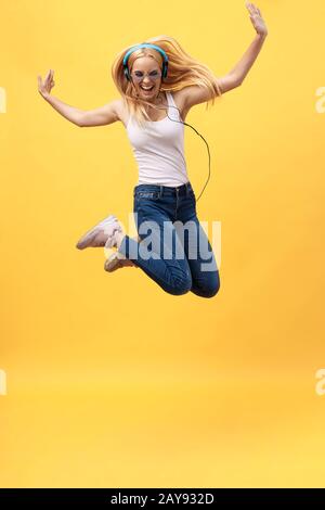 Das durchgehende Porträt einer unbeschwerten Frau in jean Jumping beim Musikhören. Innenfoto eines adligen kaukasischen weiblichen Modells in Stockfoto