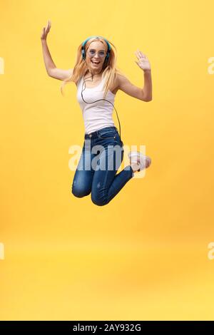 Das durchgehende Porträt einer unbeschwerten Frau in jean Jumping beim Musikhören. Innenfoto eines adligen kaukasischen weiblichen Modells in Stockfoto