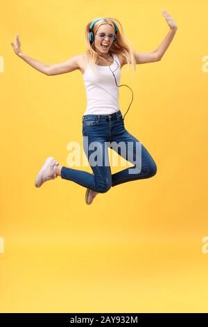 Das durchgehende Porträt einer unbeschwerten Frau in jean Jumping beim Musikhören. Innenfoto eines adligen kaukasischen weiblichen Modells in Stockfoto