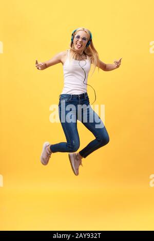 Das durchgehende Porträt einer unbeschwerten Frau in jean Jumping beim Musikhören. Innenfoto eines adligen kaukasischen weiblichen Modells in Stockfoto