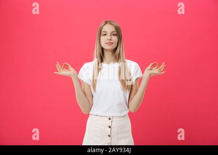 Blonde beauiful junge Frau macht Mudra-Zeichen, entspannt sich nach hartem Arbeitstag, hält die Augen geschlossen, übt Yoga gegen den rosafarbenen Rücken Stockfoto