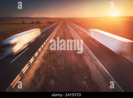 Nutzfahrzeuge in der Landstraße, dramatischer Sonnenuntergang, Bewegungsunschärfe. Fracht-, Transport- Konzept Stockfoto