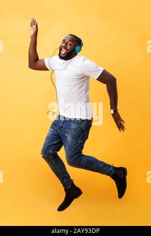 Porträt eines kirschjungen afroamerikanischen Mannes, der Musik mit Kopfhörern hört und isoliert über Gelb tanzt Stockfoto
