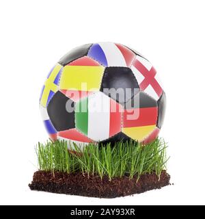 Klassischer Soccerball mit verschiedenen Flaggen, die auf einem Stück Gras liegen, das auf weißem Hintergrund isoliert ist Stockfoto