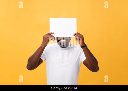 Junge happy african-american versteckt sich hinter einem leeren Papier, auf gelbem Hintergrund Stockfoto