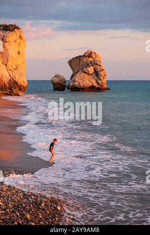 Ein Junge spielt am Strand an den Felsen Petra tou Romiou, in Paphos, Zypern. Stockfoto