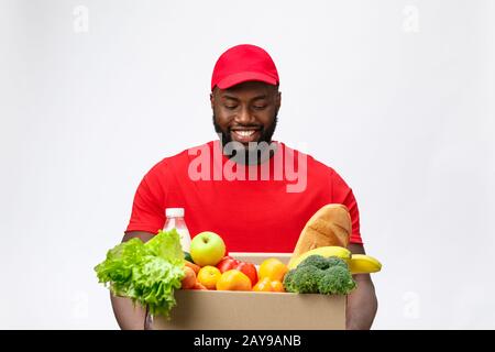 Lieferkonzept - Ein Gutaussehender afroamerikanischer Liefermann, der eine Packung Lebensmittel und Getränke aus dem Geschäft mitführt. Isoliert ein Stockfoto