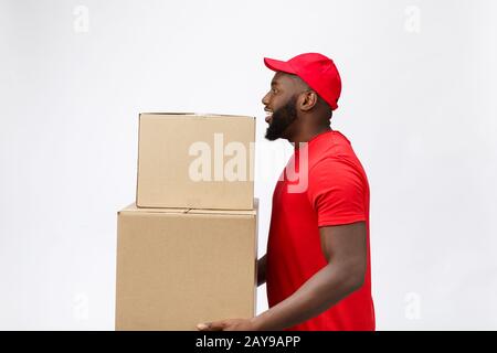 Lieferkonzept - Seitenansicht Portrait of Happy African American Delivery man in rotem Tuch, das eine Schachtel enthält. Isoliert auf Gre Stockfoto