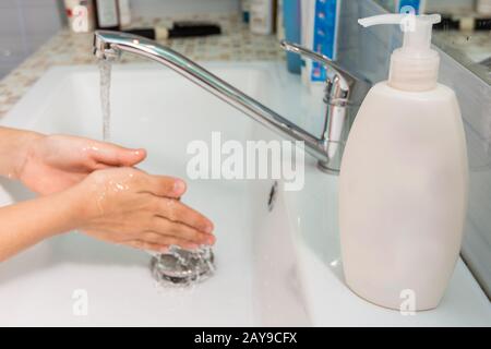 Das Kind wäscht seine Hände unter den Wasserhahn, im Vordergrund eine Tube flüssige Seife Stockfoto