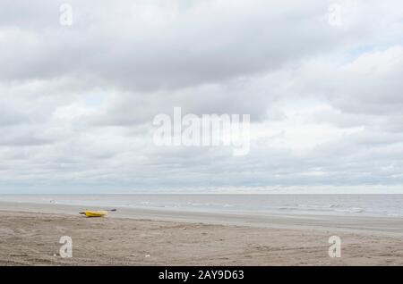 Strandlandschaft ohne Menschen, gelbes Kajak im Sand, ruhiges Meer und bewölkter Himmel, in Punta Rasa, Provinz Buenos Aires, Argentinien Stockfoto