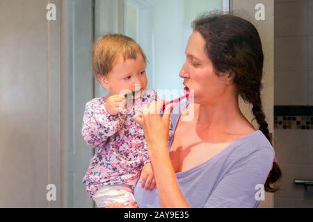 Baby lernen, wie man die Zähne putzen kann. Kleines Kind, das die Zähne mit der Mutter putzt. Baby an den Händen der Mutter, das die Zähne mit der Mutter putzt. Mutter und Tochter putzen die Zähne im Badezimmer. Stockfoto