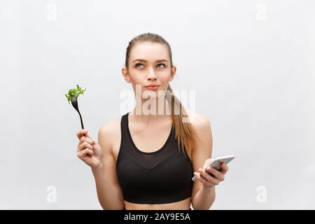 Schöne junge Frau tragen Sportliche Kleidung mit Salat in der Hand, mittels Smart Phone. Stockfoto