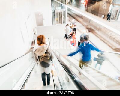 Entschärfte Sicht mit verschwommenen Silhouetten von Menschen auf Rolltreppe und U-Bahn-Plattform innerhalb der Metrostation von Barcelona Stockfoto