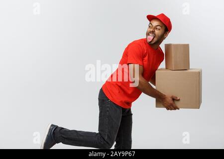 Lieferkonzept - Ein Ansehnlicher afroamerikanischer Liefermann, der für die Lieferung eines Pakets für den Kunden hetzt. Isoliert auf Grau s Stockfoto