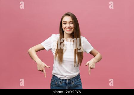 Foto der glückliche junge Frau stehen und poiting Finger über rosa Hintergrund isoliert. Stockfoto