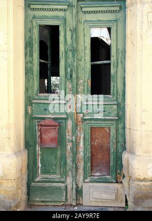 Zerbrochene alte doppelgrüne Türen in einem verlassenen derben Haus mit zerbrochenen Fenstern Stockfoto